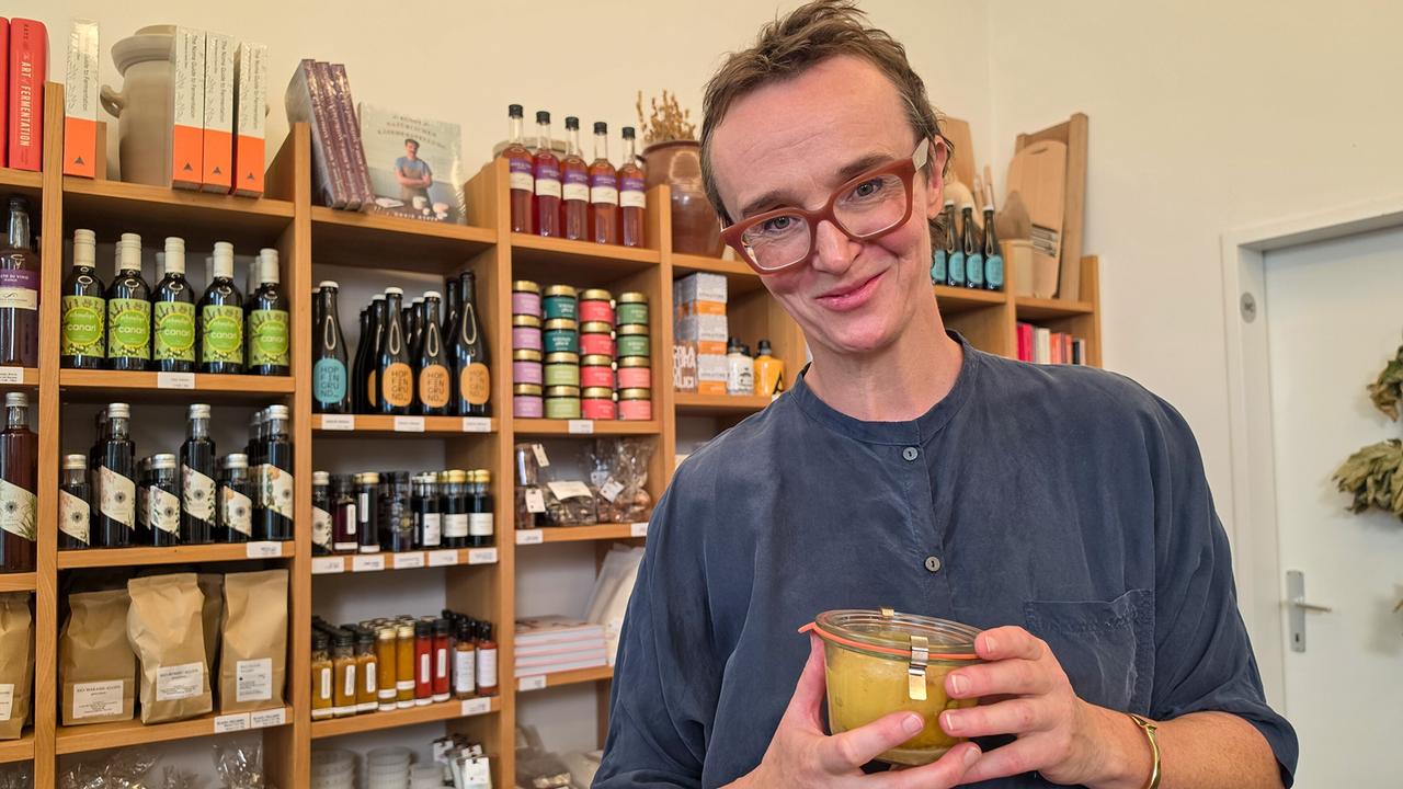 Alexandra Liberda steht in ihrem Wiener Geschäft vor einem Verkaufsregal und hält ein Glas fermentiertes Gemüse.