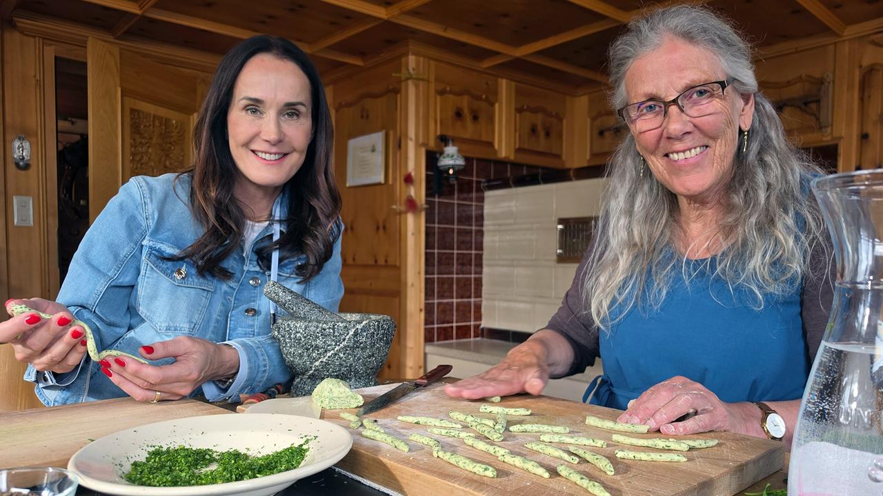 © ORF/Ab Hof TV Produktion Angelika Thaler-Zugg und Maggie Entenfellner formen Teigstängele auf einem Holzbrett in der Küche.