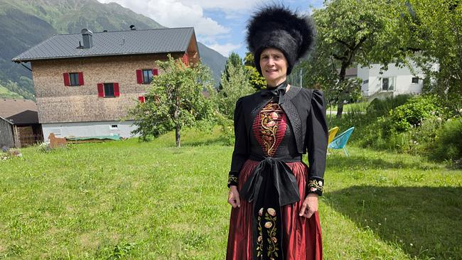 © ORF/Ab Hof TV Produktion Kerstin Keßler in Montafoner Tracht mit traditionellem Mäßli auf einer Wiese vor Bauernhäusern.