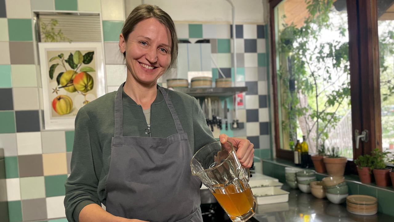 © ORF/Ab Hof TV Produktion Maria Kinzl in der Küche des Café Schillwasser mit einem Krug Gundermann-Sirup