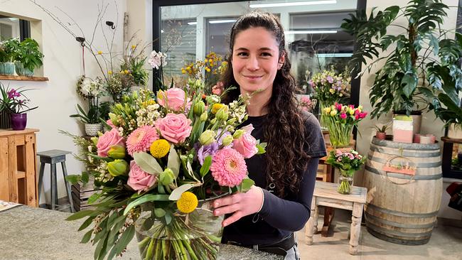 Gärtnerin Lisa Wagner hält stolz einen großen Frühlings-Blumenstrauß in der Hand.