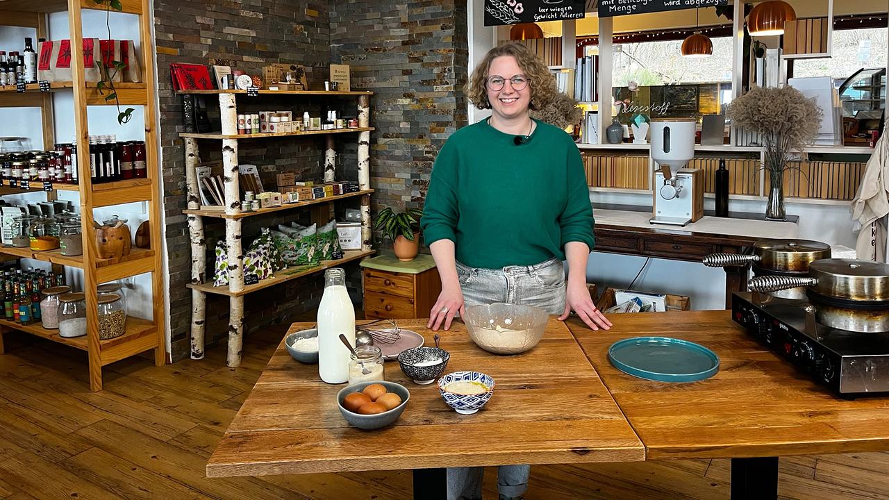 Carmen Schachinger steht im Unverpackt-Laden und Café hinter einem Holztisch mit Schüssel, Milch, Eiern und weiteren Zutaten