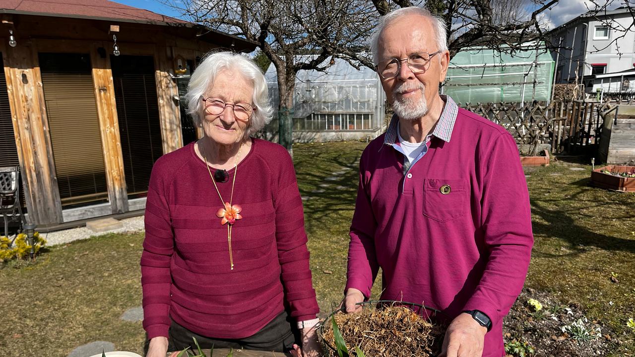 Regina und Adolf Koffler stehen an einem Tisch mit Orchideenpflanzen im Garten.