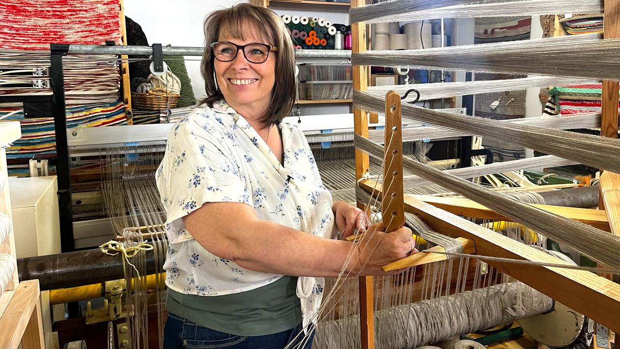 © ORF/Ab Hof TV Produktion Helga Holzer am Webstuhl in ihrer Werkstatt mit gewebten Textilien im Hintergrund.