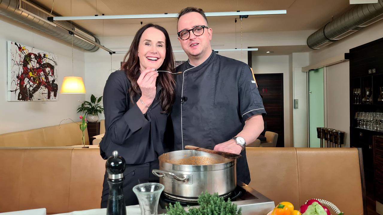 Maggie Entenfellner und Andreas Ruckendorfer stehen nebeneinander hinter einem großen Kochtopf