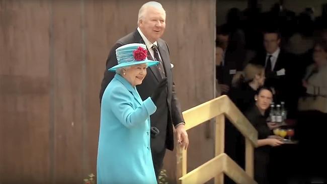 Queen Elizabeth in einem blauen Kleid und Hut beim lächeln und winken. 