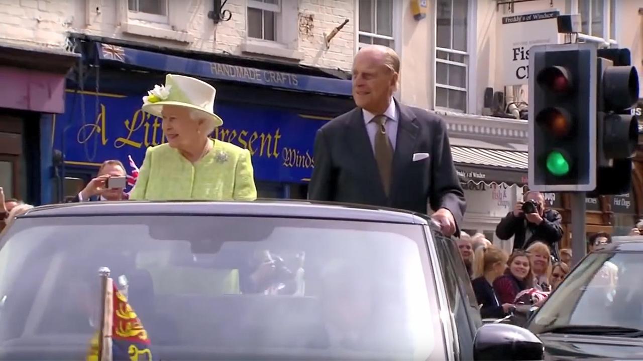 Queen Elizabeth und Prinz Philip stehend, bei einer Parade, in einer Limosine mit offenem Veredeck. 