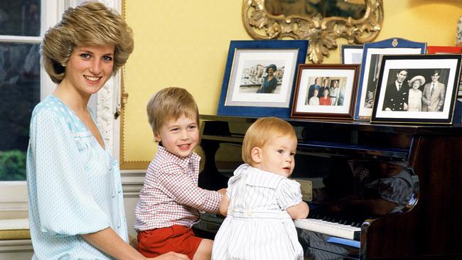 Eine junge Prinzessin Diana und ihre beiden Söhne William und Harry als Kinder sitzen an einem Klavier und lächeln in die Kamera. 