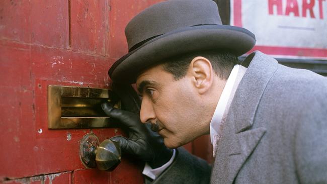David Suchet (Hercules Poirot) schaut durch den Briefschlitz einer roten Tür.