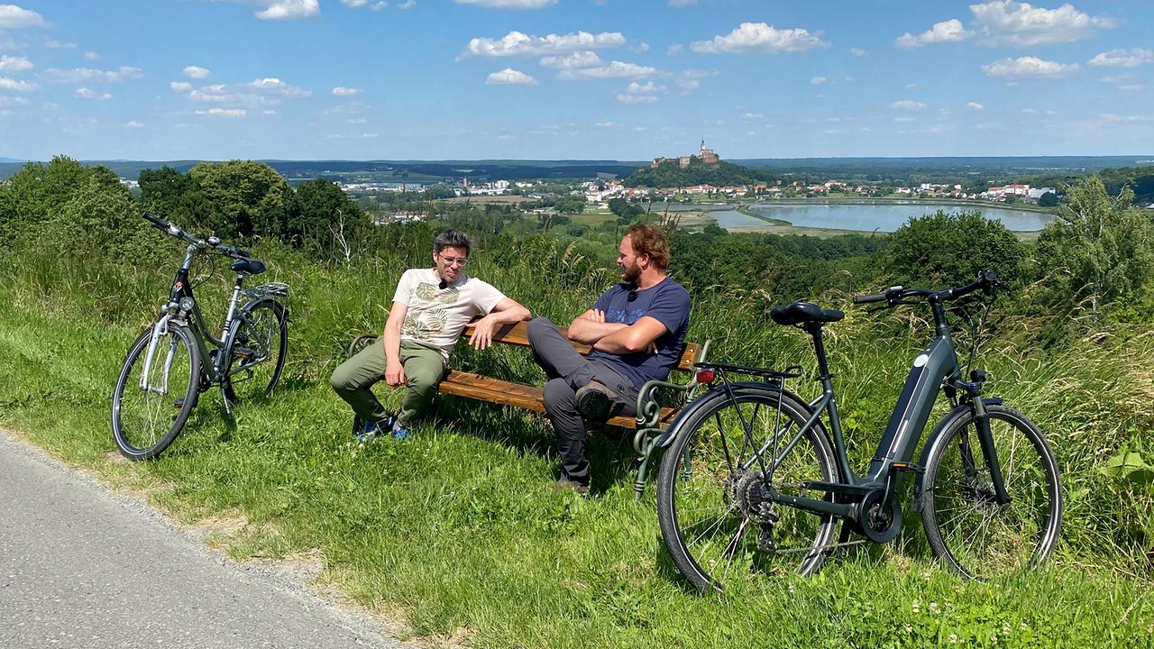 © ORF/splash productions Andreas Jäger und Thomas Sitipsits machen auf eine Bank Pause von ihrer Radtour im Südburgenland.