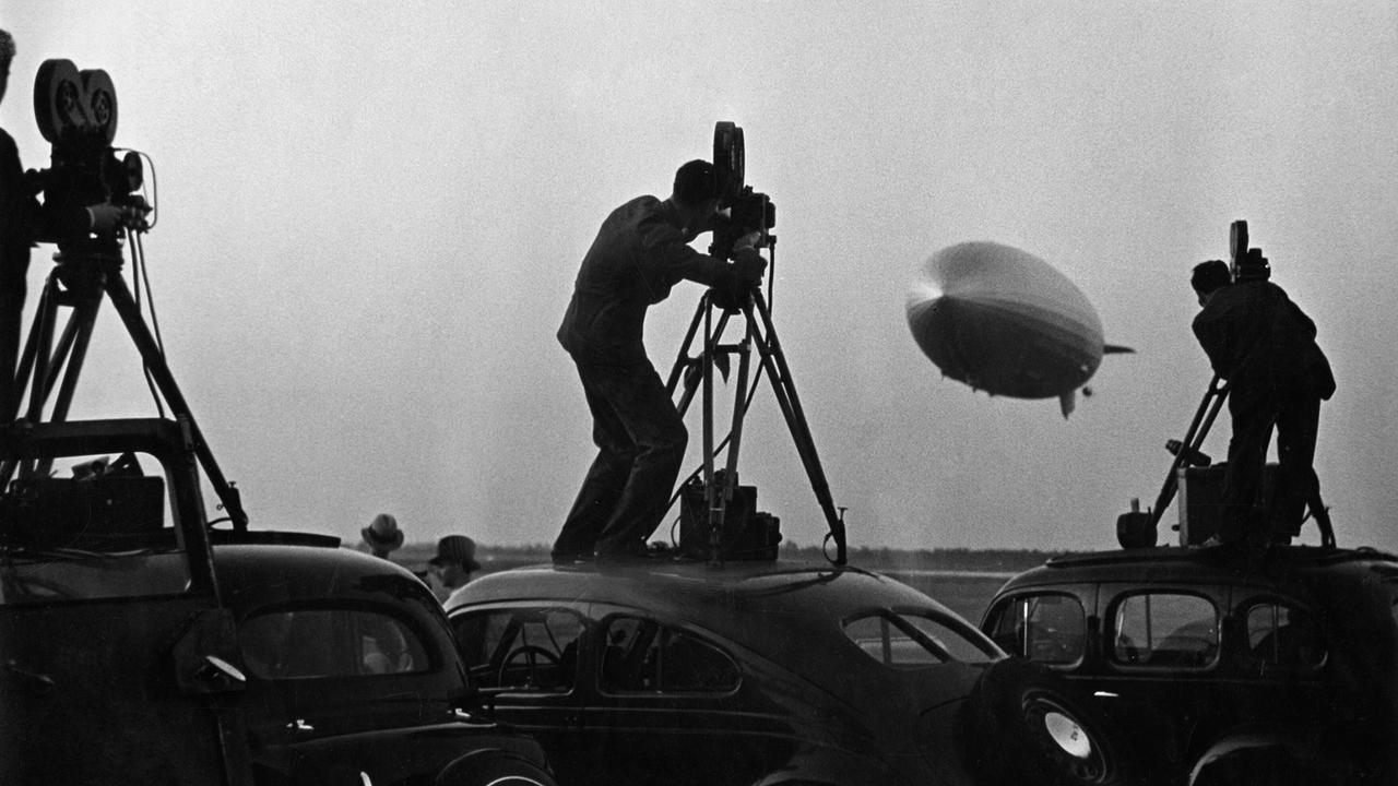 Kameraleute stehen auf Autodächern und filmen die Rückkehr der "Hindenburg" nach ihrer Nordatlantik-Fahrt, 01.01.1936.