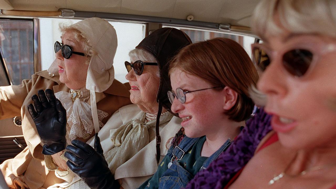 © ORF/Wega Film/Petro Domenigg Gusti Wolf, Jane Tilden, Sarah Veit und Dolores Schmidinger sitzen mit auffälligen Brillen und Kopfbedeckungen dicht nebeneinander in einem Auto.