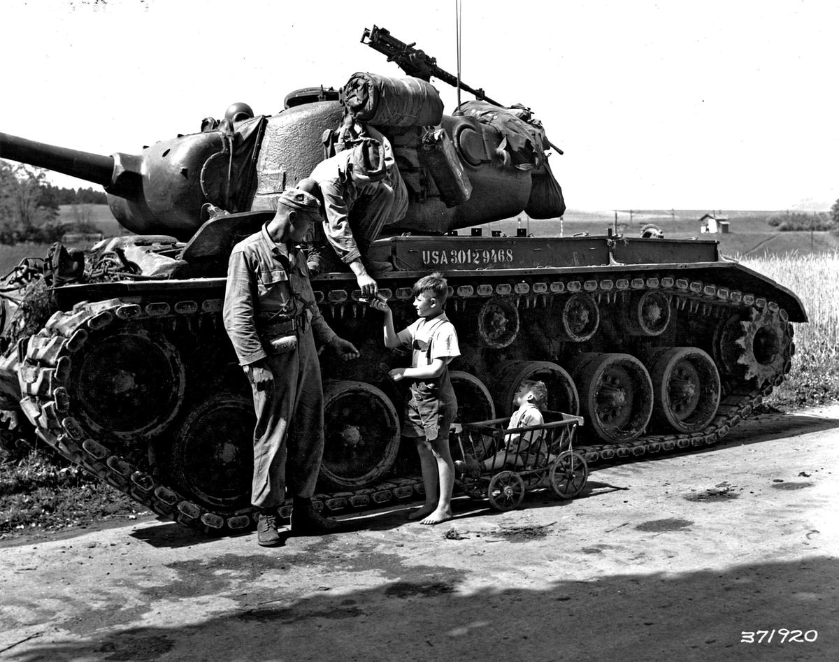 Österreich 25.05.1951 - Übung "Rebound": Sgt. Donald A.Ziesmer (Kalispell, Montana) und Sgt. William P. Kratzenberg (Pittsburg, Pa), Mitglieder der Medium Tank Company, 350th Infantry Regiment, verschenken Süssigkeiten an zwei österrreichische Kinder, die ihren Panzer bewundern.
