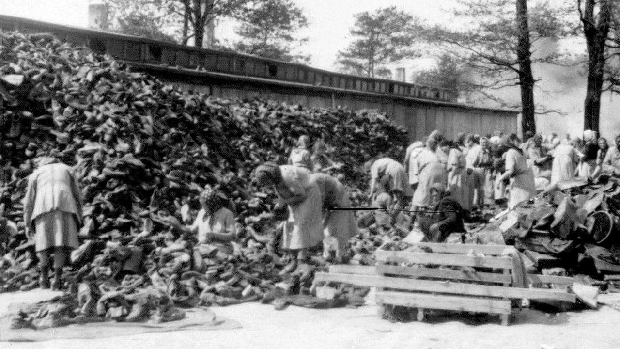 Die Habe der Menschen, deren Transport „abgefertigt“ wurde wird im Materiallager „Kanada“ von Häftlingen sortiert. Im Hintergrund qualmt eine Grube, in der Leichen verbrannt werden.