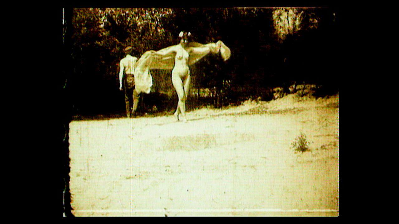 Szene aus dem Film "Sandbad" (1906) - Saturn Film. Eine nackte Frau tanzt auf einer Wiese.