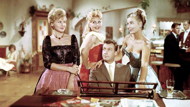 Im Weißen Rössl (Komödie, 1960); Im Bild: Peter Alexander sitzt am Klavier. Neben ihm steht Waltraut Haas, hinter ihm zwei weitere junge Damen. Alle lächeln.