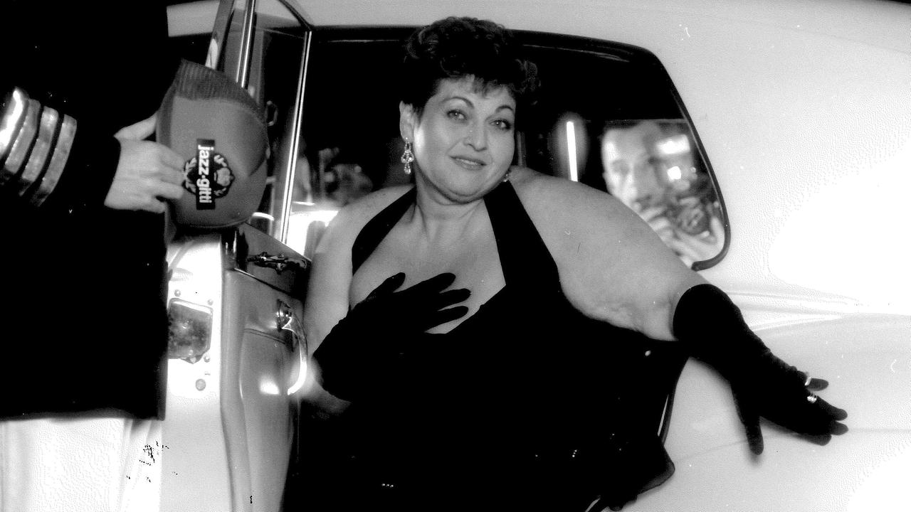 Schwarzweiß-Foto von Jazz Gitti in einem eleganten Kleid steigt aus einem klassischen Auto aus, während jemand die Tür für sie aufhält.