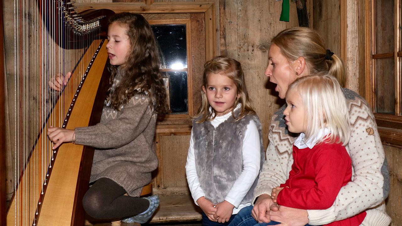 Familie Hölzl beim Musizieren. Ein Mädchen spielt die Harfe, eine Frau und zwei kleinere Mädchen singen.