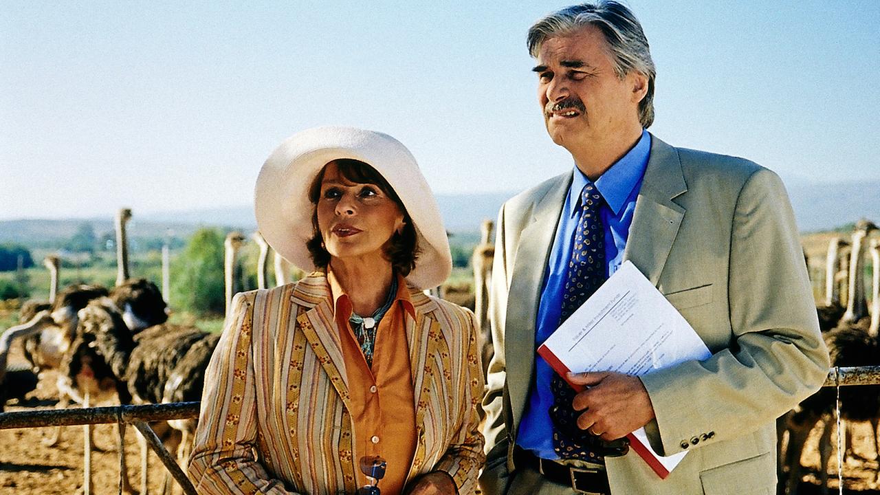 Senta Berger und Peter Simonischek stehen nebeneinander. Hinter ihnen Straußen einer Straußenfarm.