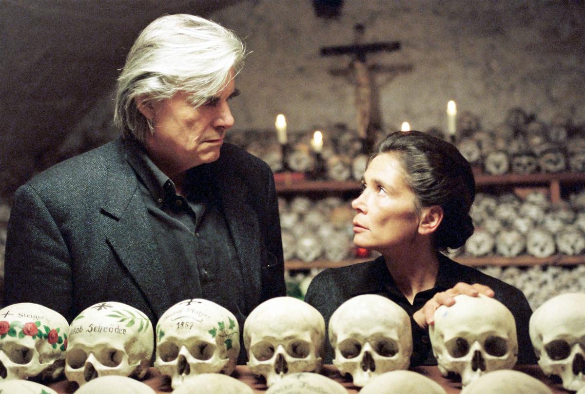 Peter Simonischek (Daniel Käfer) und Birgit Doll (Frau Gamsjäger) stehen in einer Kammer unter der Erde, die voller Totenköpfe ist.