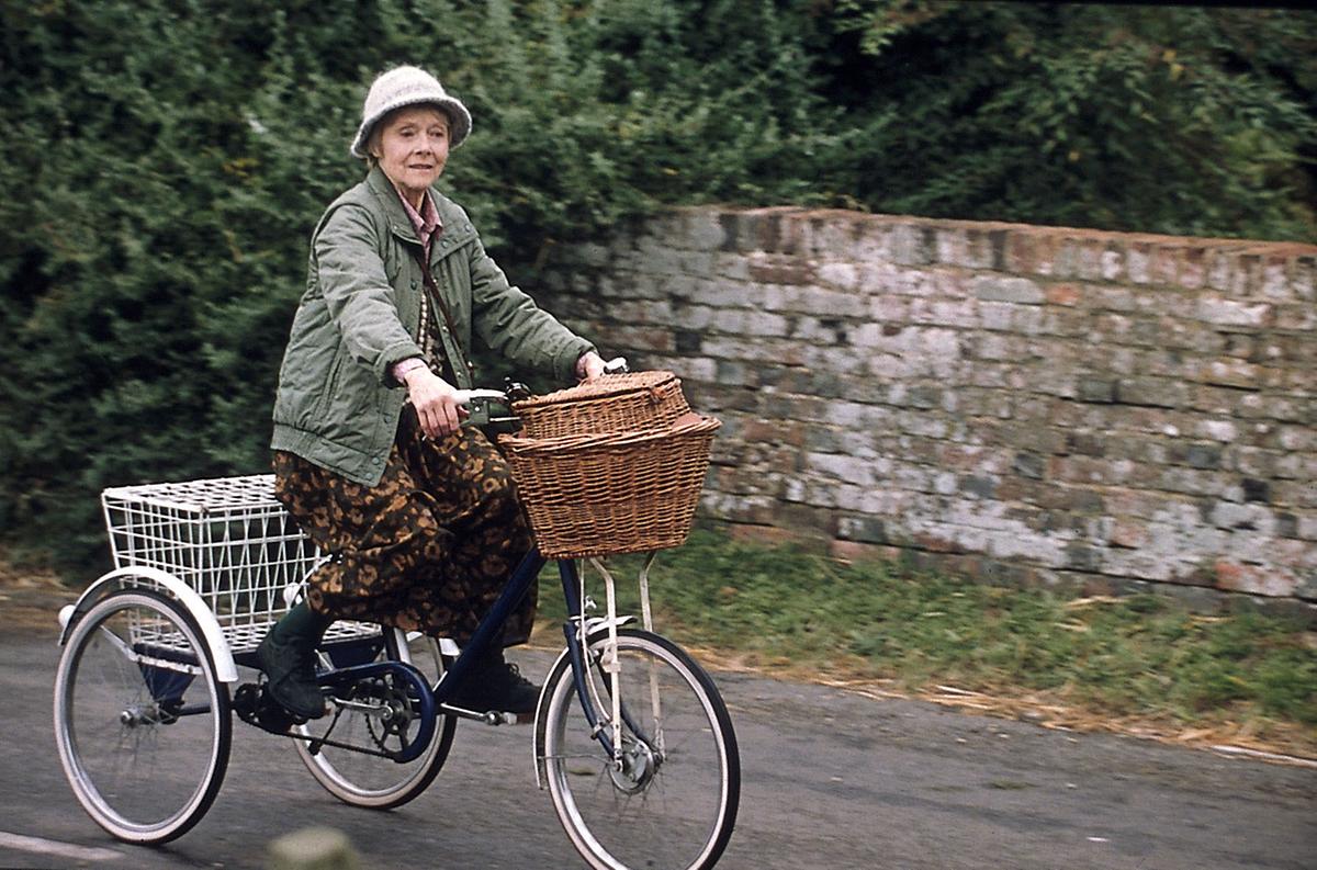 Die pensionierte Lehrerin Emily Simpson (Renee Asherson) fährt mit einem 3-rädrigen Fahrrad.