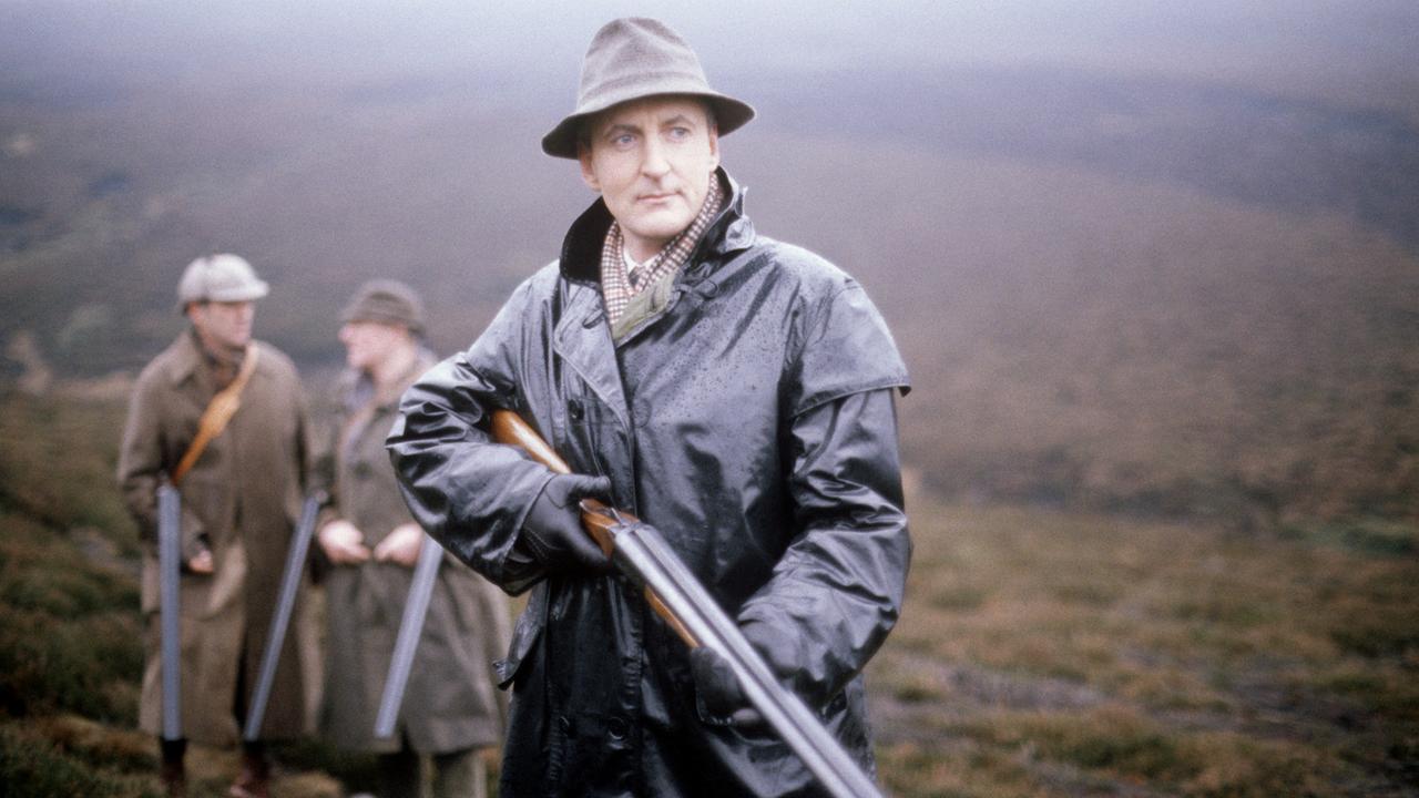 Agatha Christie’s Poirot: Geheimnisvoller Mord im Jagdhaus (Originaltitel: Poirot "The Mystery of Hunter's Lodge" (GB 1991)), Im Bild: Hugh Fraser (Captain Haistings) steht mit einem Gewehr in einem Feld; hinter ihm zwei Männer, die sich unterhalten.