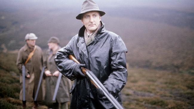 Agatha Christie’s Poirot: Geheimnisvoller Mord im Jagdhaus (Originaltitel: Poirot "The Mystery of Hunter's Lodge" (GB 1991)), Im Bild: Hugh Fraser (Captain Haistings) steht mit einem Gewehr in einem Feld; hinter ihm zwei Männer, die sich unterhalten.