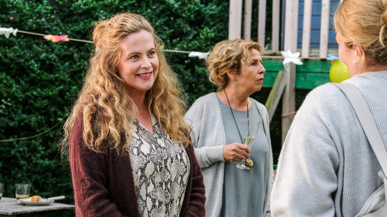 Bei einer Gartenfeier unterhalten sich Anne Sandmeier und Barbara Bauer, während Michalea May mit einem Glas Sekt daneben steht.
