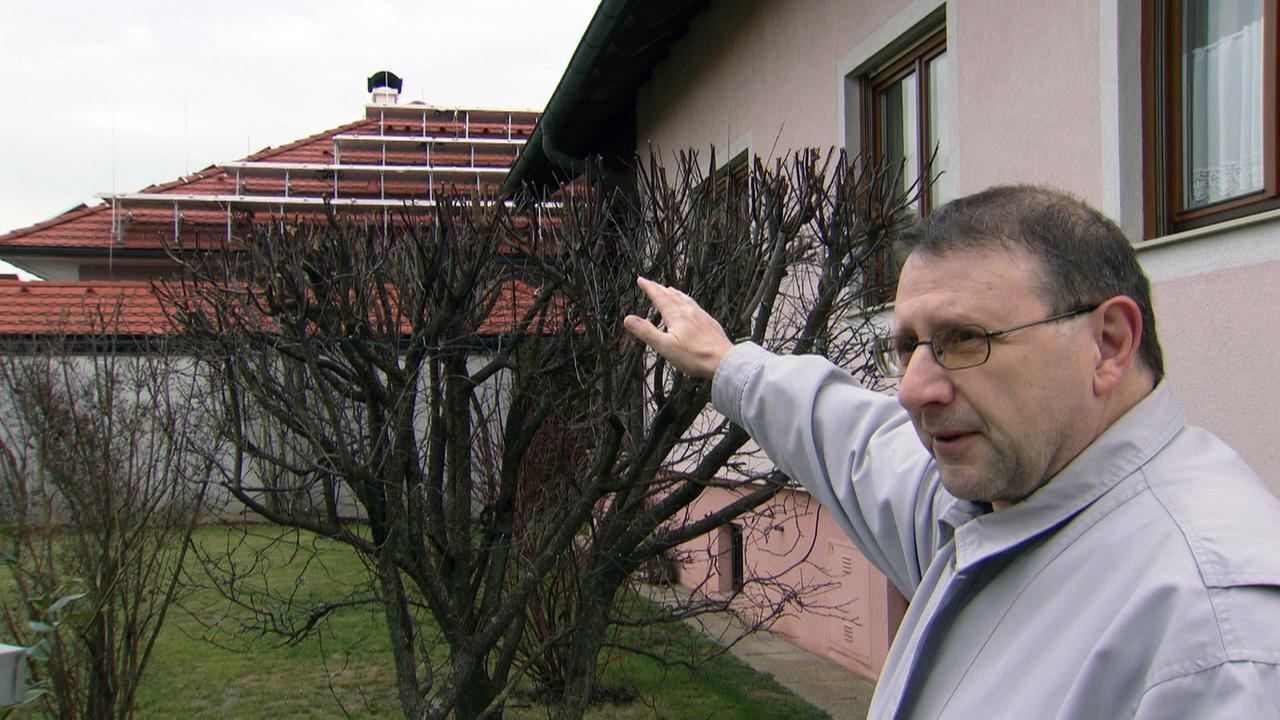 ein Herr vor seinem Haus, zeigt mit Finger auf die Photovoltaik von seinem Nachbar