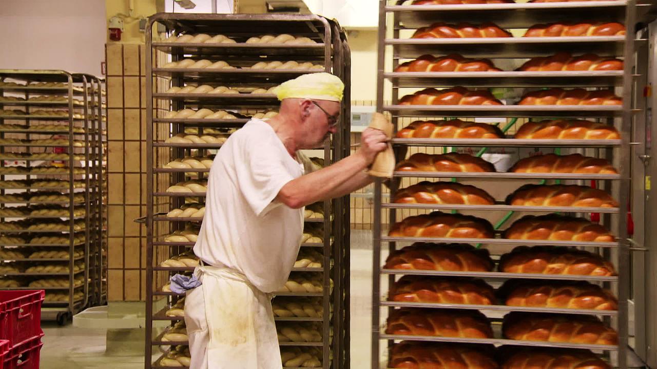 Ein Bäcker in der Backstube schiebt ein Blech voller Strietzel