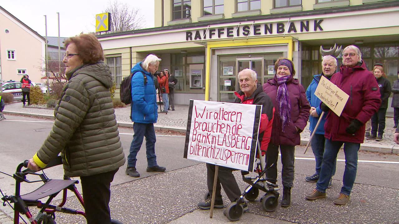 Pensionist im Rollstuhl mit einem Schild auf dem steht: "Wir alten brauchen die Bank in Lasberg. Bitte nicht zusperren." 