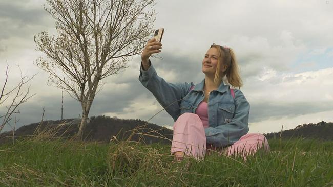 Gini Lampl alias Billie Steirisch sitzt im Gras und macht ein Selfie