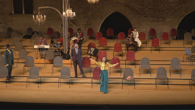 Isabelle Huppert steht vor Stühlen in einer Pluderhose und einer Bluse auf der Bühne zu „La Cerisaie"