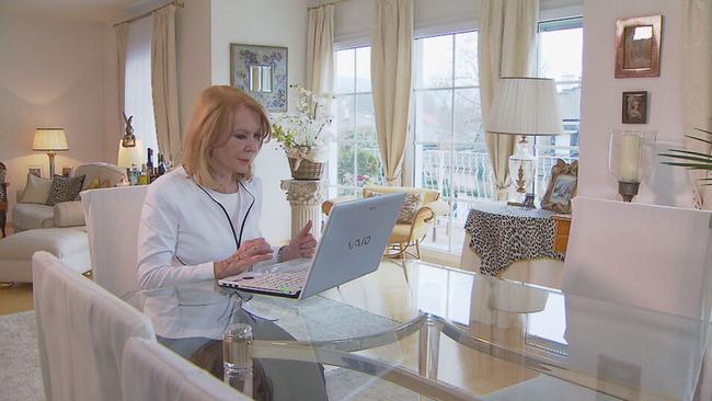 Astrologin Gerda Rogers sitzt an einem Glastisch in einem Wohnzimmer. Vor ihr steht ein Laptop