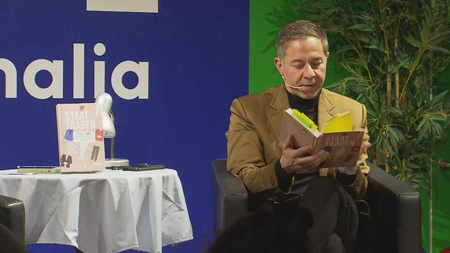 Autor Daniel Kalt sitzt mit dem Buch in der Hand auf der Bühne und liest vor 
