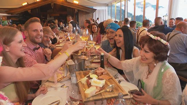 © ORF / Seitenblicke Gäste sitzen mit Essen an einer langen Tafel und prosten sich mit Weingläsern zu