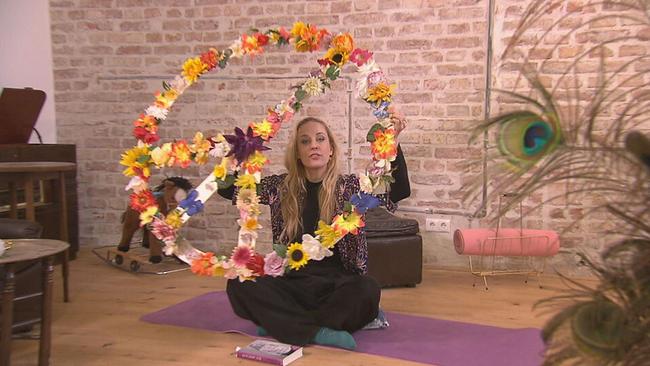 Lilian Klebow sitzt mit einem Peacezeichen aus Blumen auf dem Bodem in ihrem Atelier