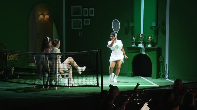 Jaye Simmons steht mit einem Tennisschläger in der Hand auf der Bühne