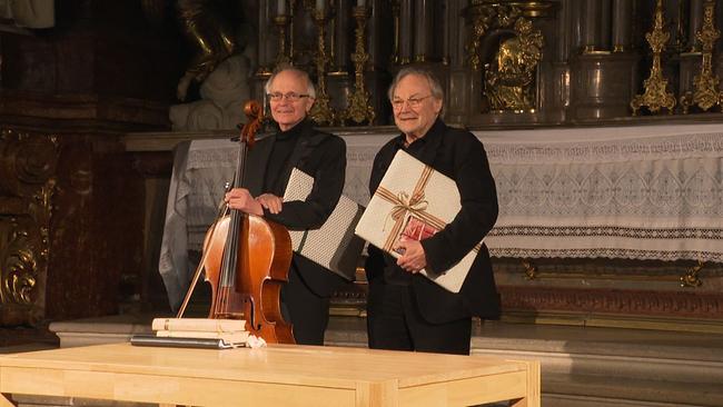 Franz Bartolomey steht mit Chello neben Klaus Maria Brandauer vor dem Altar