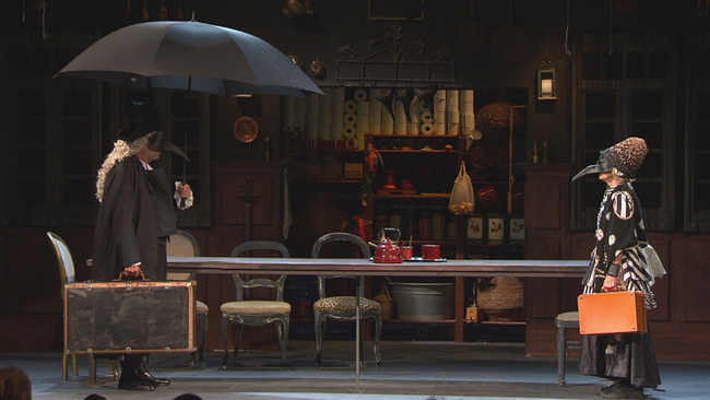 Zwei Schaupieler mit Koffer in der Hand und schwarzem Schnabel im Gesicht stehen sich auf der Bühne des Lustspielhauses gegenüber