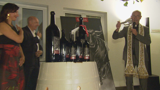 Dompfarrer Toni Faber steht vor Flaschen die auf einem Weinfass stehen. Er segnet diese vor den Gästen 