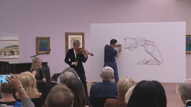 Yury Revich steht mit Geige auf der Bühne, hinter ihm wird ein abstraktes Bild gezeichnet
