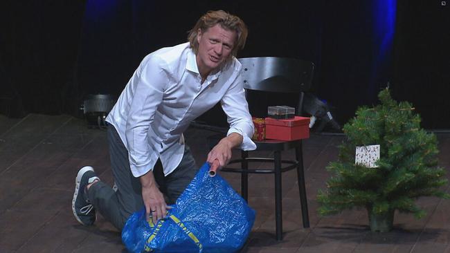 Kabarettist Gery Seidl kniet mit Weihnachtsgeschenkpapier auf dem Boden vor einem Christbaum
