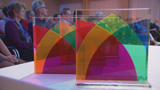 Der Fundraising Award steht auf einem Tisch. Es ist eine viereckige, stehende Glasplatte darin 5 verschiedene Farben die einer Blume ähneln. 