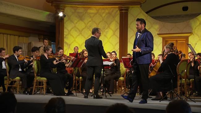 Clemens Unterreiner steht singend auf der Bühne vor einem Orchester