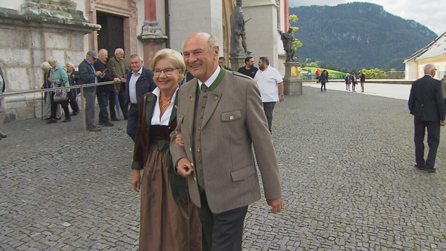 Erwin Pröl und Frau Elisabeth gehen in Trachtenkleidung an der Kirch in Mariazell vorbei 