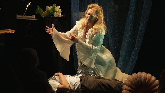 Salome Darstellerin Elena Schreiber kniet vor einem Mann, der am Boden liegt und dessen Kopf mit einem schwarzen Tuch bedeckt ist