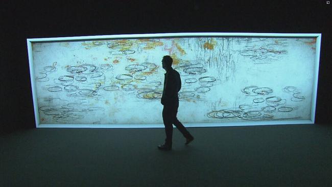 Ein Man geht an einem großen Screen vorbei der ein bewegtes Kunstwerk von Monet zeigt (Seerosen etwas abgeändert) 