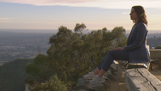 Kathrin Beck sitzt auf Felsmauer und blickt auf Los Angeles