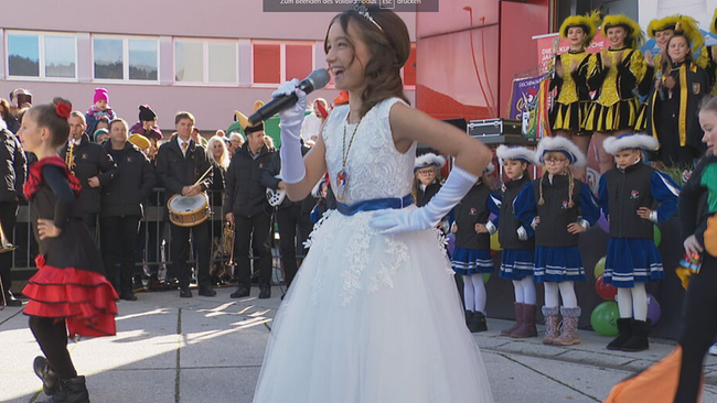 Marie in einem weißen Kleid mit Mikro in der Hand
